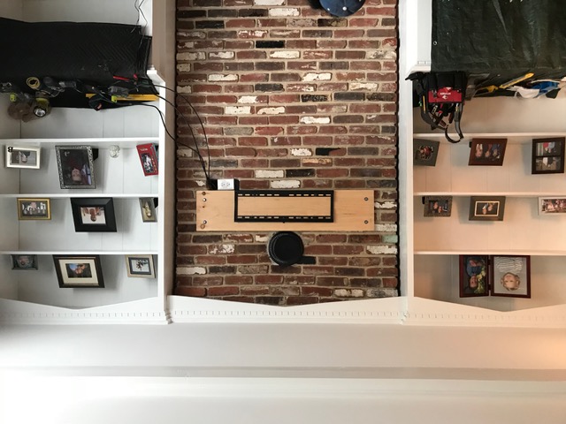 TV mount in progress on brick accent wall with built-in shelves in NJ